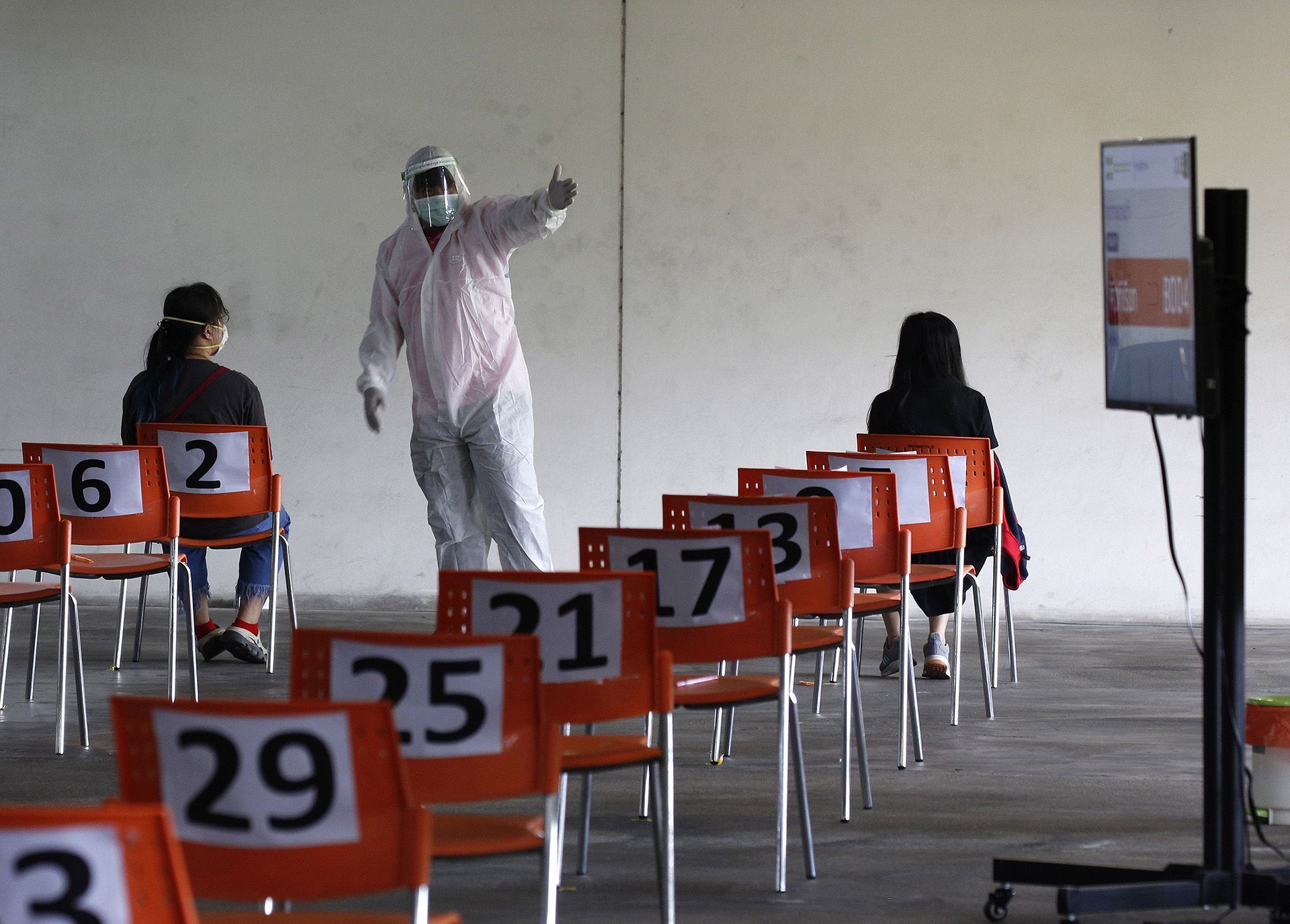 Védőruhát viselő egészségügyi alkalmazott beszélget a számozott széken ülő, koronavírusteszt elvégzésére várakozó emberek egyikével a bangkoki Csulalongkorn Egyetem Egészségügyi Központjában 2020. március 31-én (fotó:MTI/EPA/Narong Szangnak)
