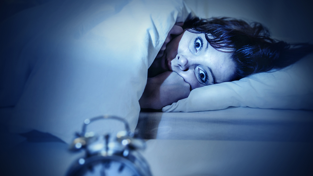 young woman in bed with alarm clock and eyes opened suffering insomnia and sleep disorder thinking about his problem on dark studio lighting in sleeping and nightmare issues