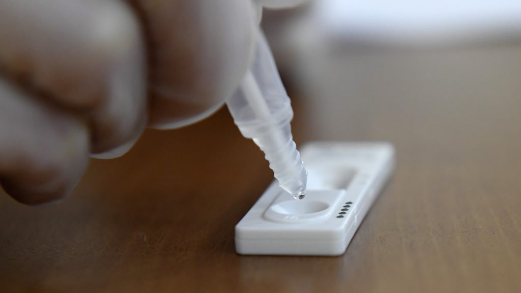 Koronavírusteszt végzése közben mintát cseppentenek az antigén gyorsteszt paneljére.