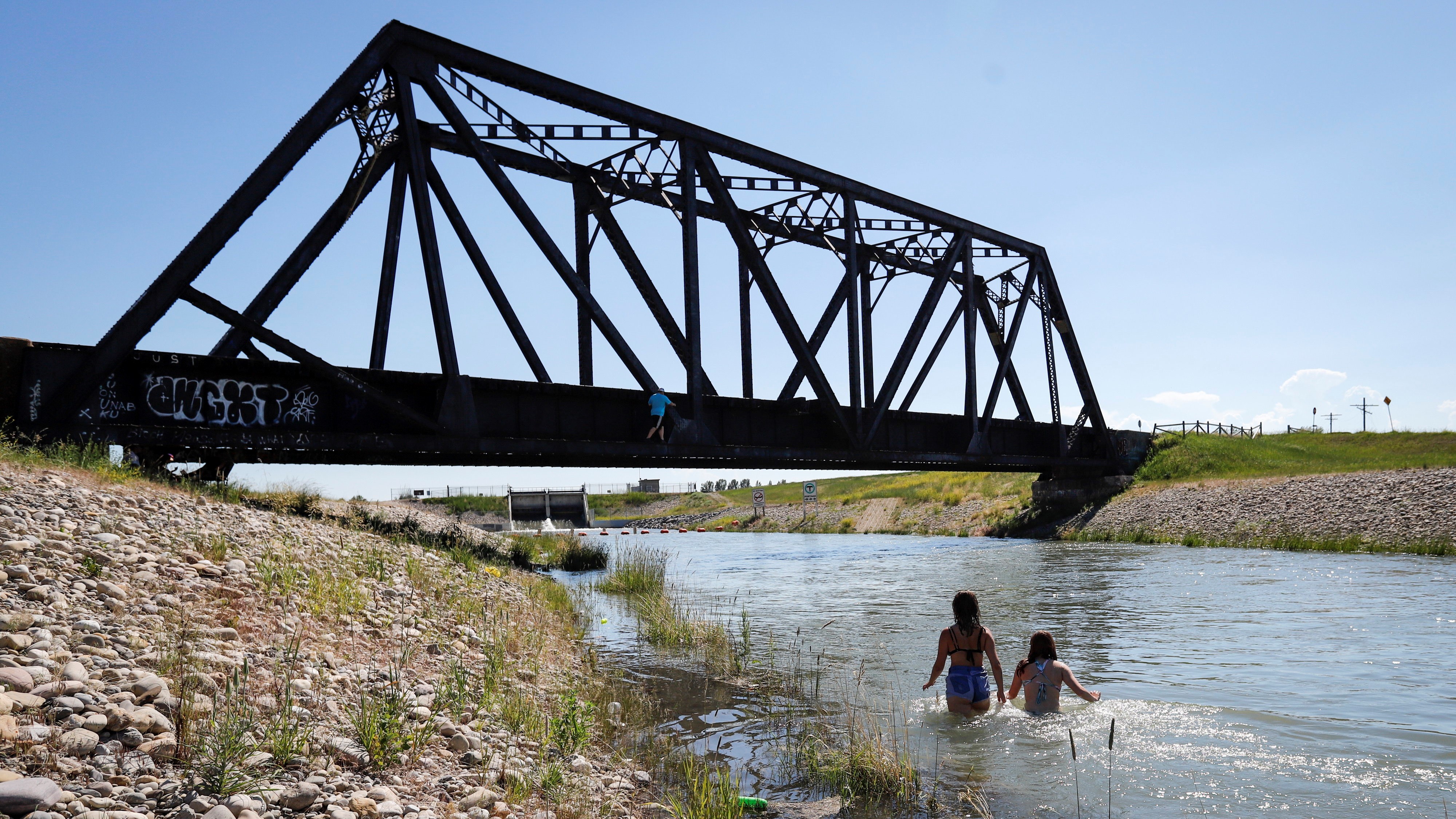Két fiatal lehűti magát egy öntözőcsatornában a kanadai Chestermere-ben 2021. június 29-én. Előző nap több mint 46 Celsius-fokkal megdőlt a hőmérsékleti rekord az országban