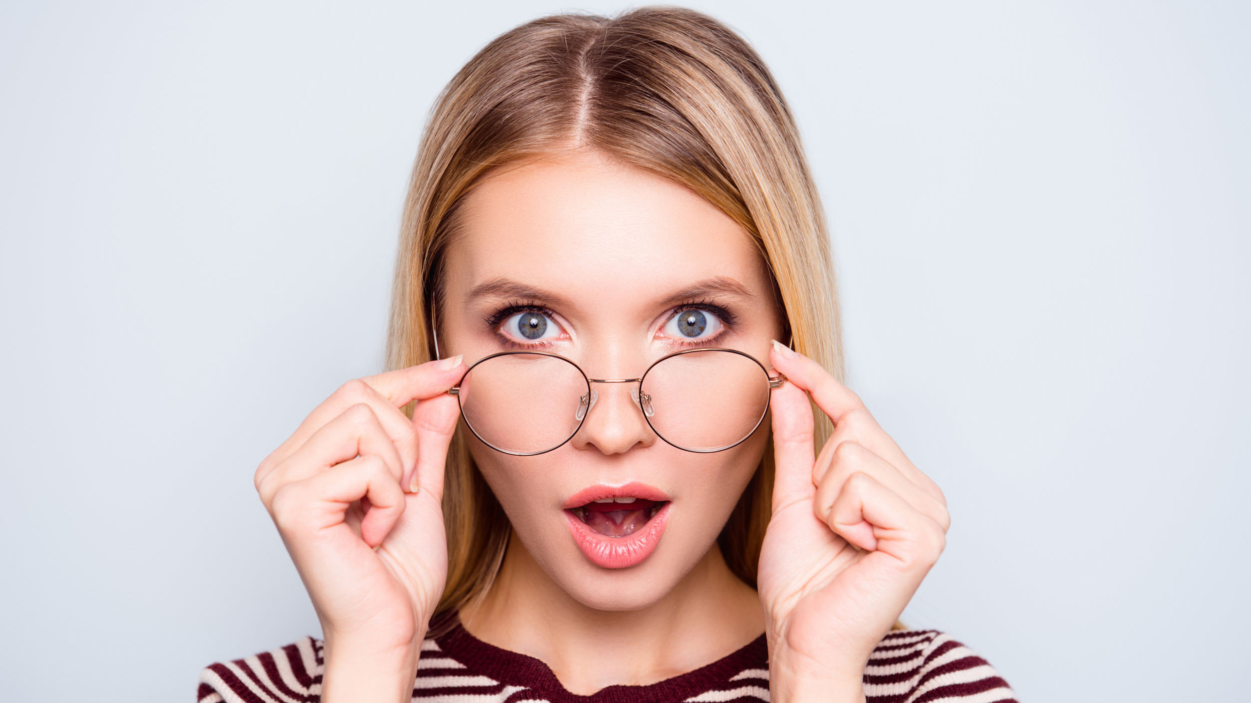 Wow! I don't believe you! Close up portrait of shocked astonished woman with open mouth and big eyes, she is touching her spectacles