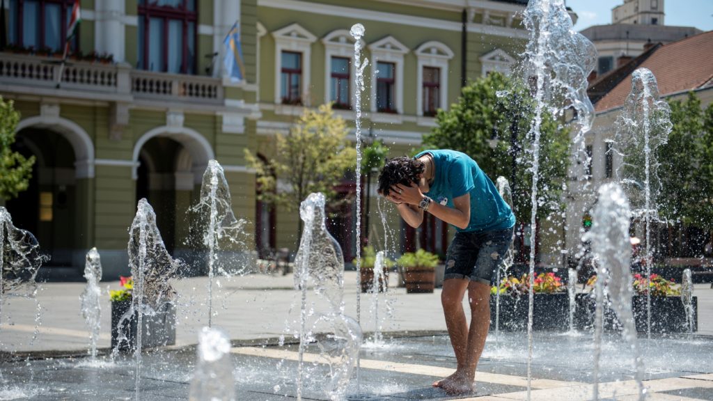 Szökőkútban frissíti magát egy férfi a hőségben az egri Dobó téren