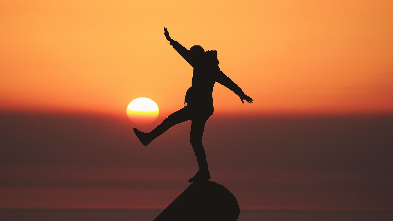 Fél lábon a sziklán álló ember naplementében