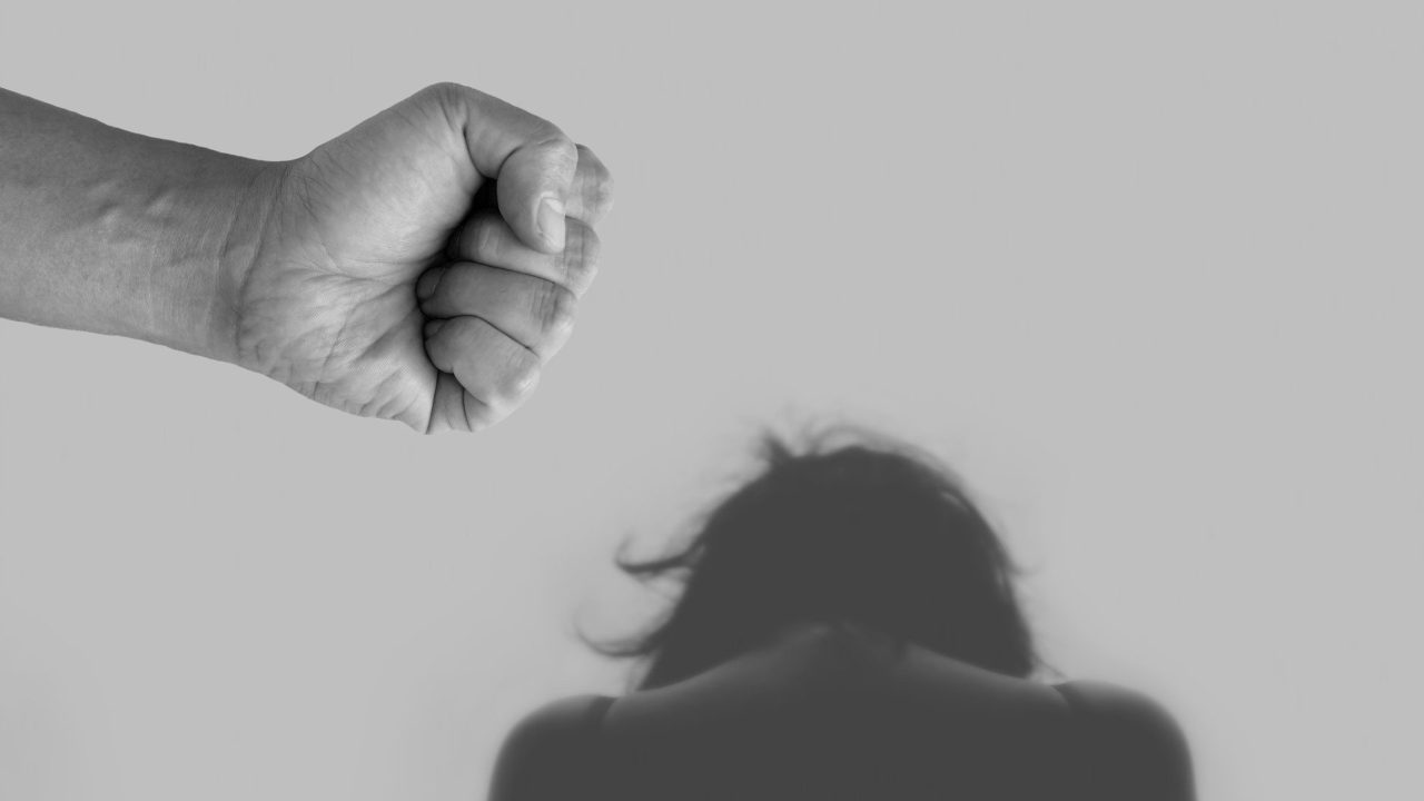 Ököllel fenyeget valaki egy háttal ülő nőt.