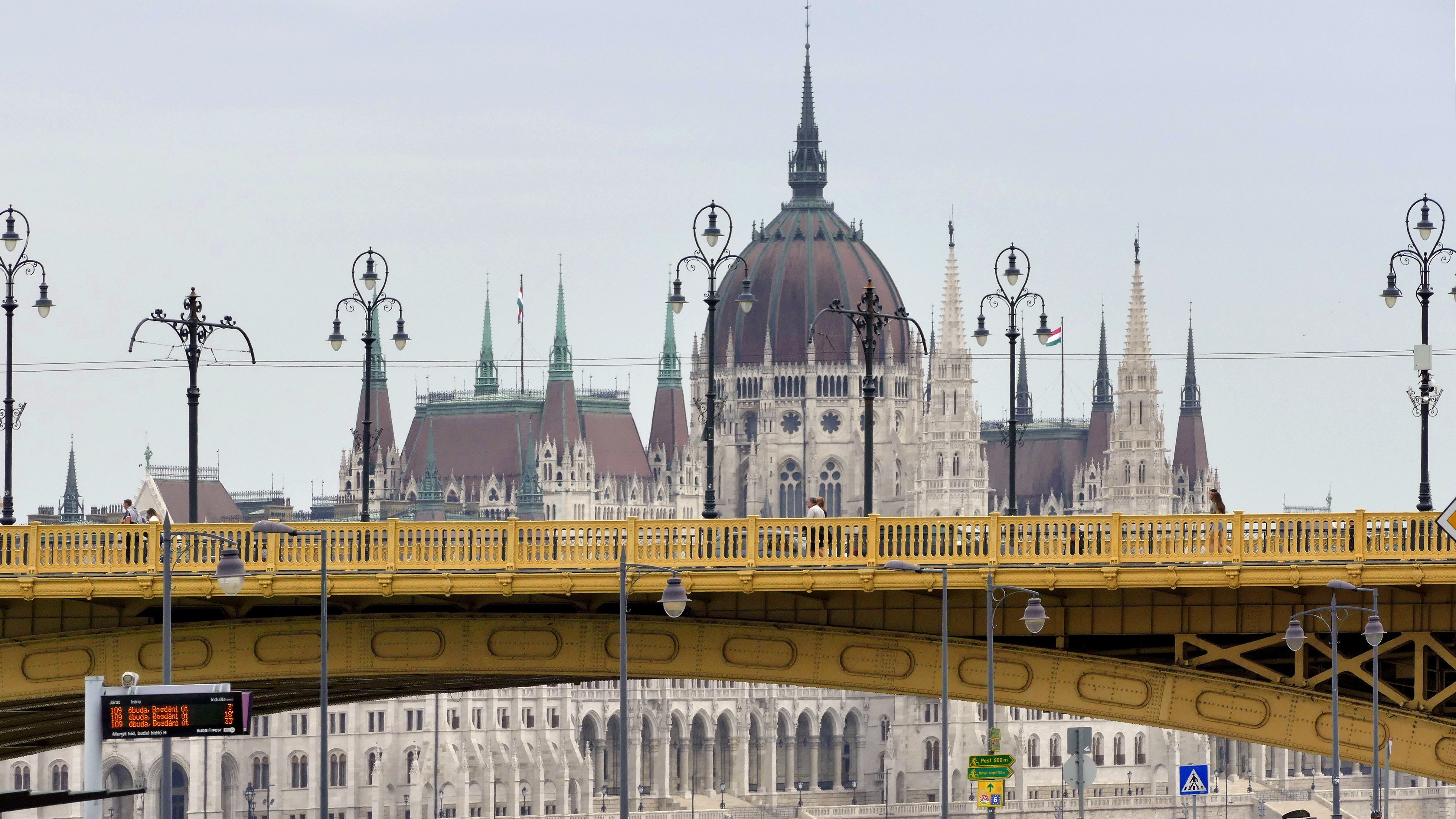 Kora délutáni járműforgalom a főváros II. kerületében az Árpád fejedelem útján, a Margit hídnál. Háttérben a Parlament épülete a Duna folyó túlpartján