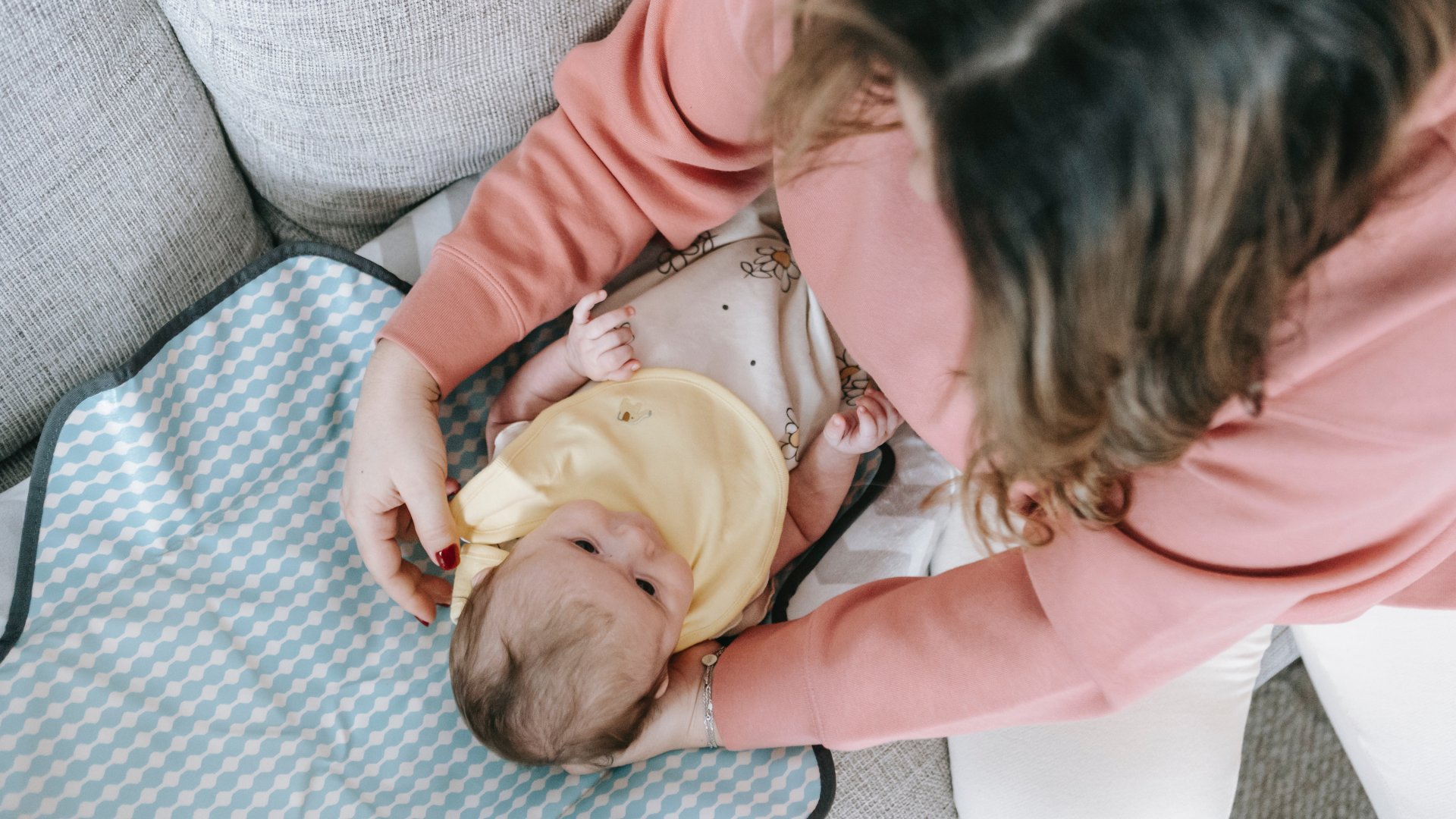 Egy nő leteszi a kanapéra a kisbabát