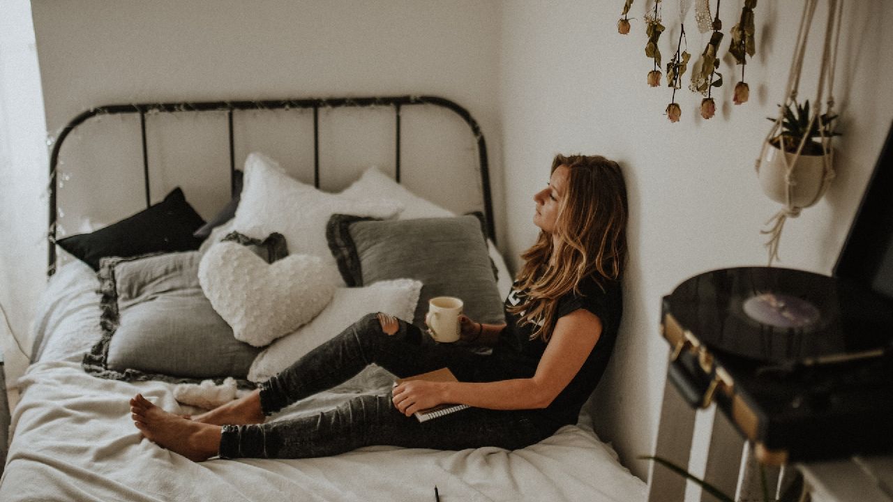 Lány ül egy ágyon csészével