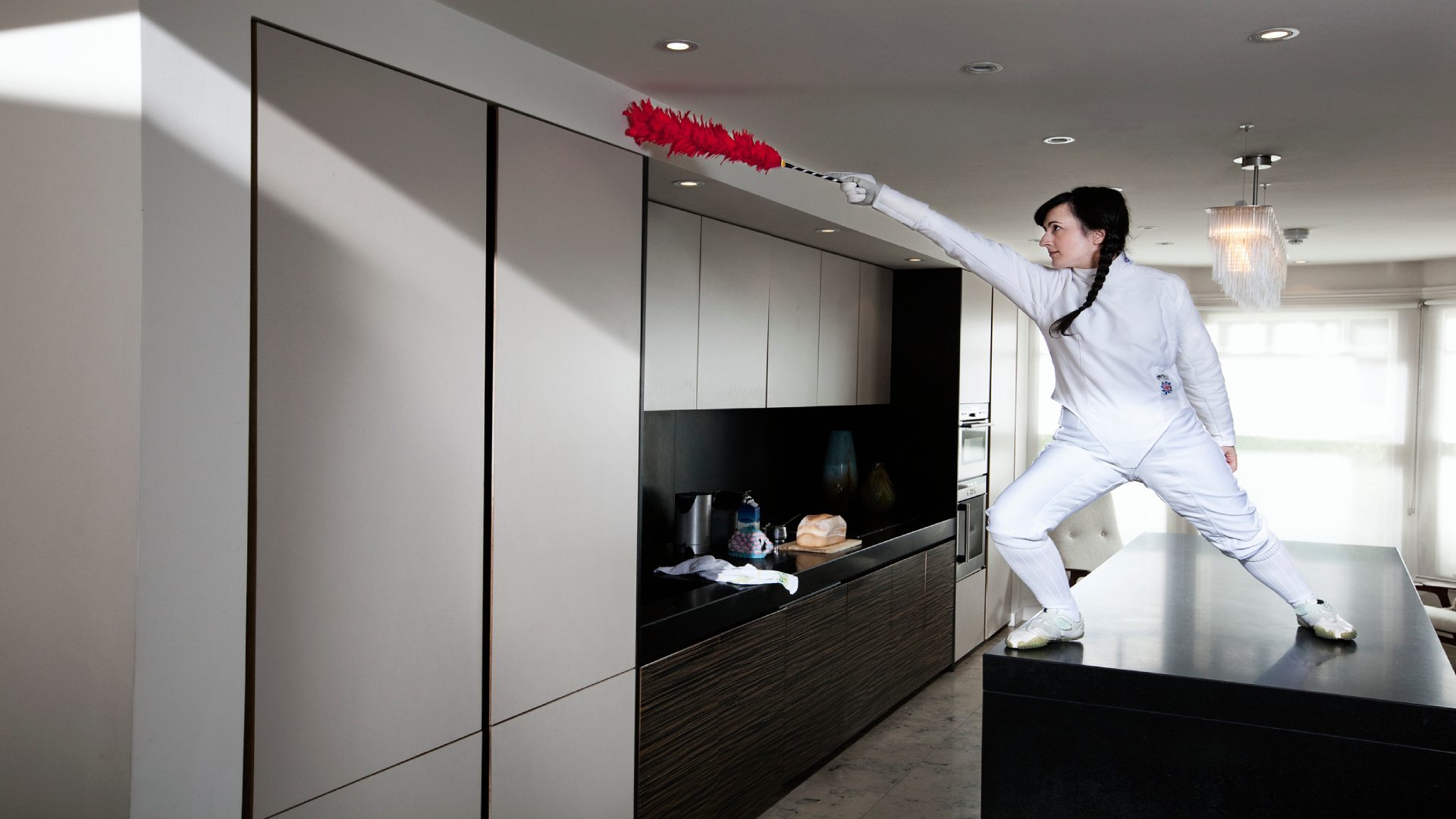 Konyhapulton álló, vivóruhás nő, portörlővel a kezében.