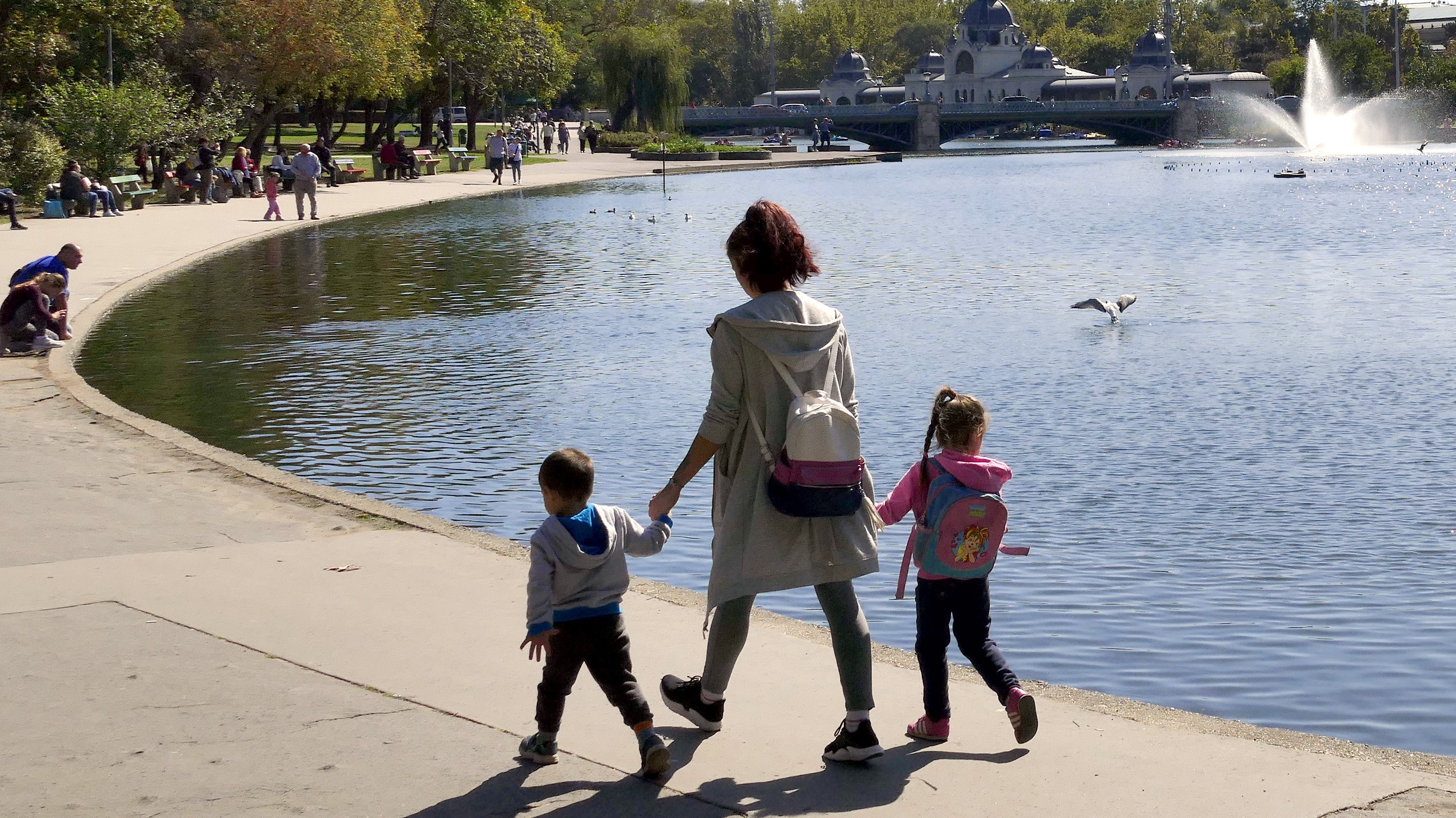 Egy édesanya két gyermekével sétál a Városligeti-tó partján kora őszi napsütésben. 