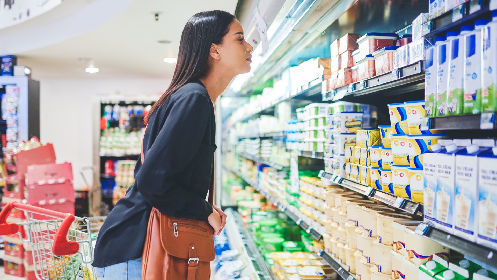 Tejtermékes polc előtt gondolkodó nő.