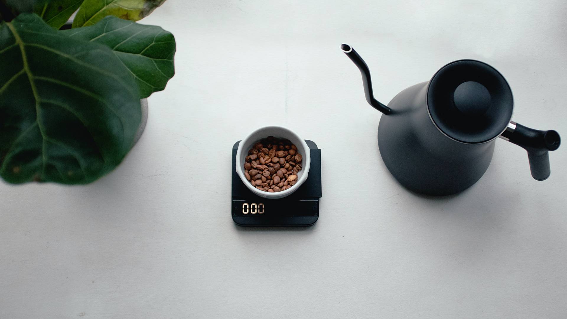 Kávészemek mérlegen és egy fekete kancsó.