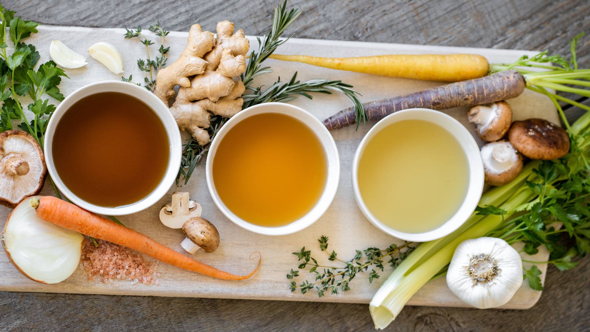 Csontleves fehér tálakban, vágódeszkán zöldségekkel.