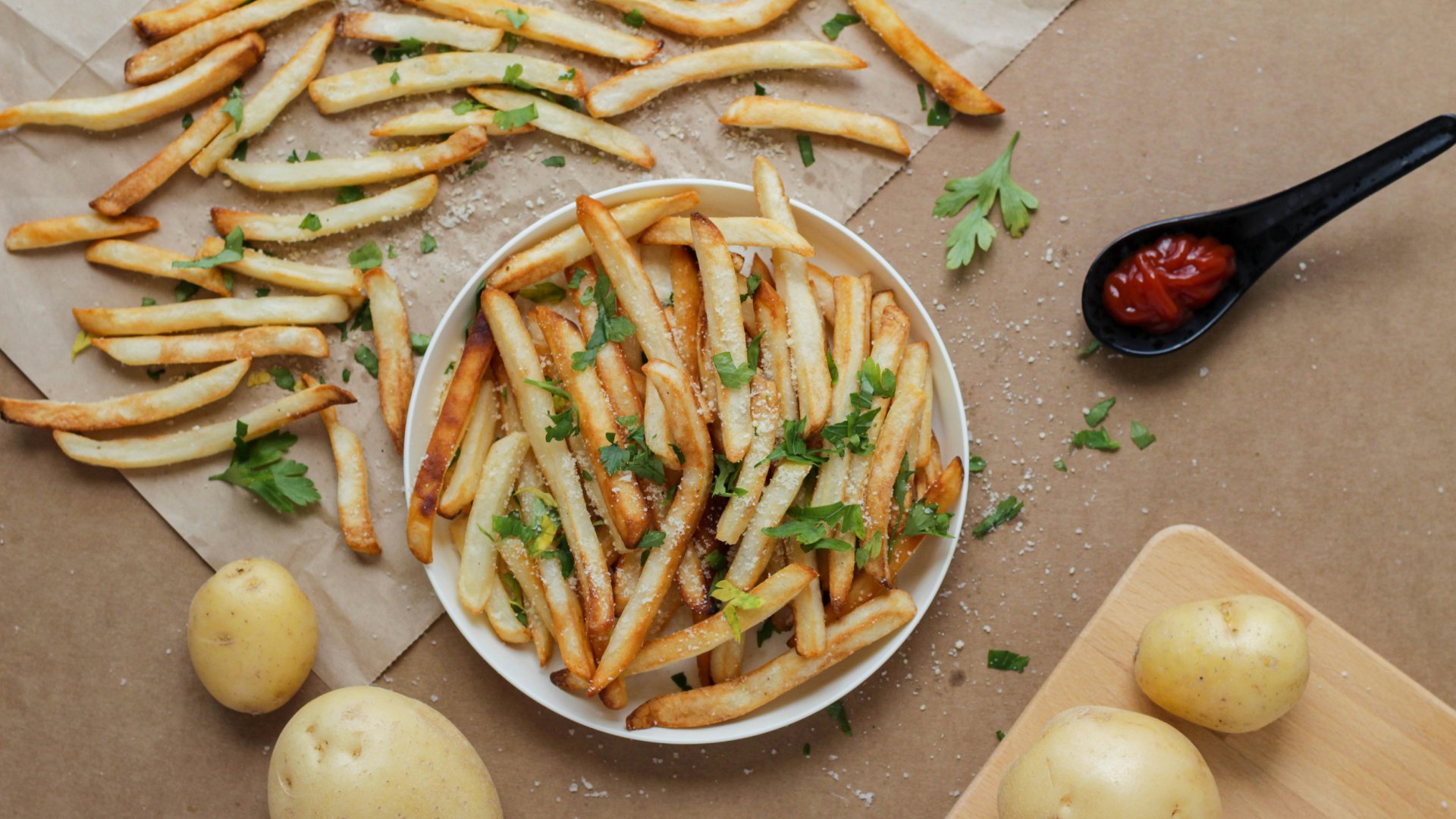 Egy tál sültkrumpli, körülötte elszórva még több sültkrumpli, ketchup és egész krumplik.