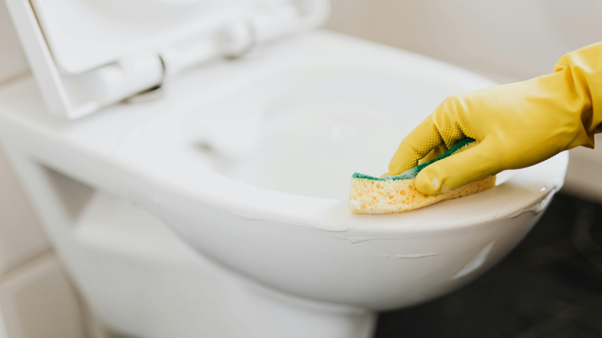 Egy nő gumikesztyűben takarítja a vécécsészét