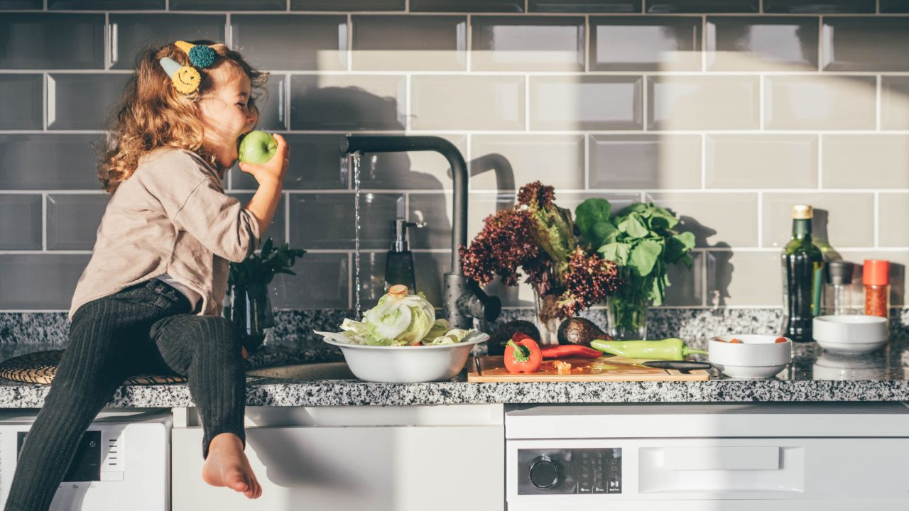 Kislány mosott almába harap a konyhapulton