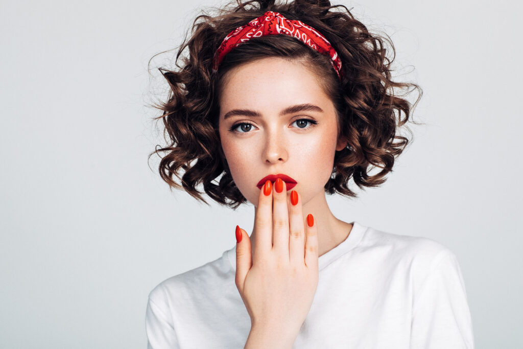 Fiatal, göndör hajú nő narancssárga körömlakkal