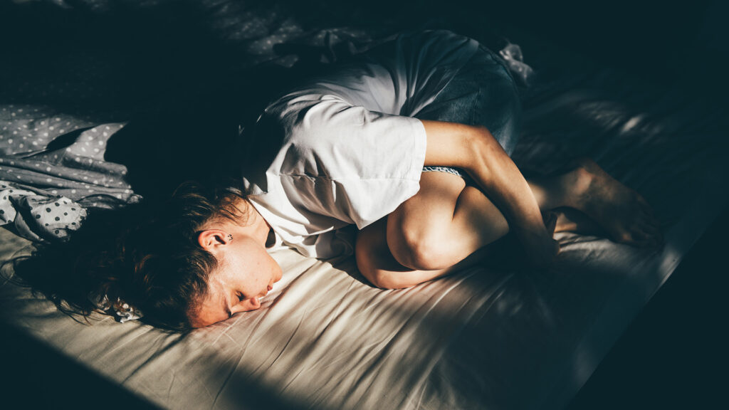 Nő összekuporodik az ágyon