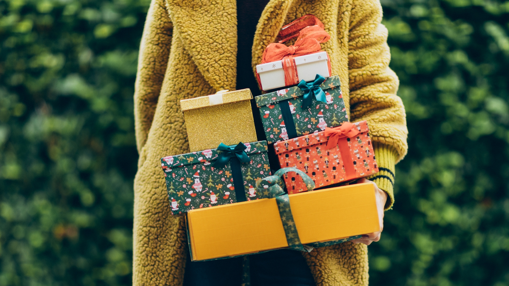 Karácsonyi ajándékok egy sárga kabátot viselő nő kezében