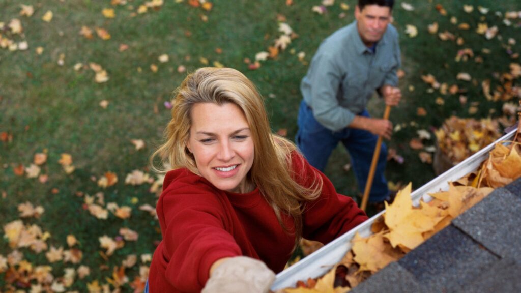 Nő tisztítja az ereszcsatornát.