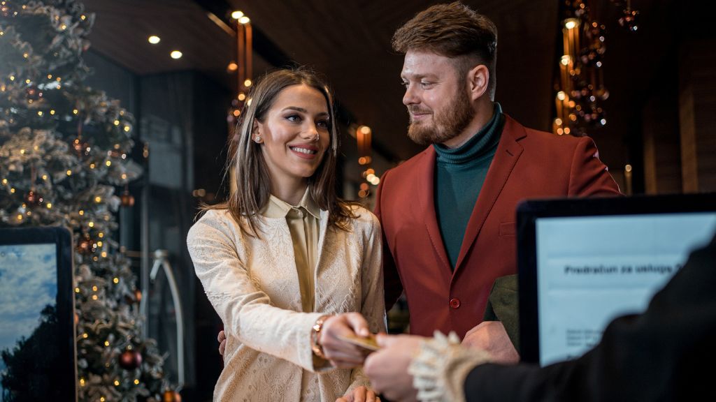 Egy szerelmes pár jelentkezik be egy hotel recepcióján karácsonykor karácsonyfával a háttérben