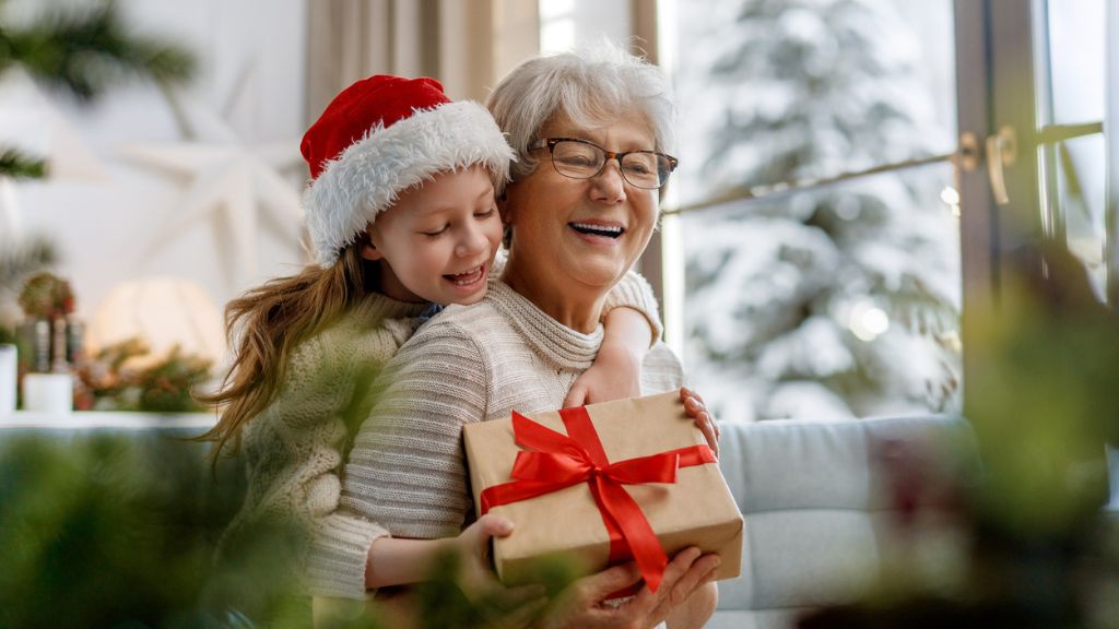 Kisgyerek átöleli a nagymamát akinek karácsonyi ajándékot ad