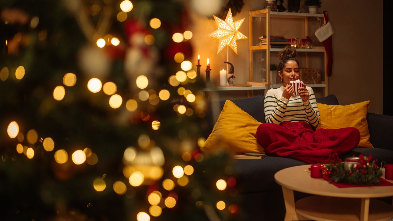 Nő ül a kanapén karácsonyfa mellett