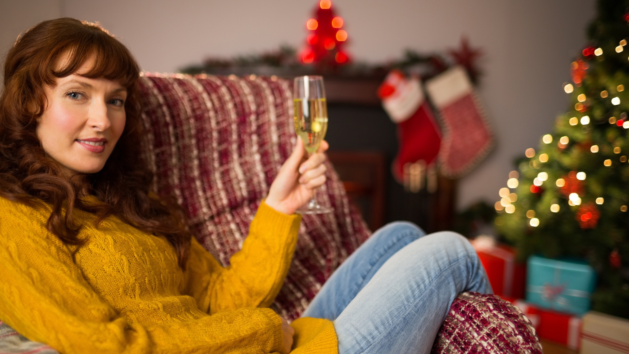 Nő ül pezsgővel a kezében a kanapén, háttérben a karácsonyfa
