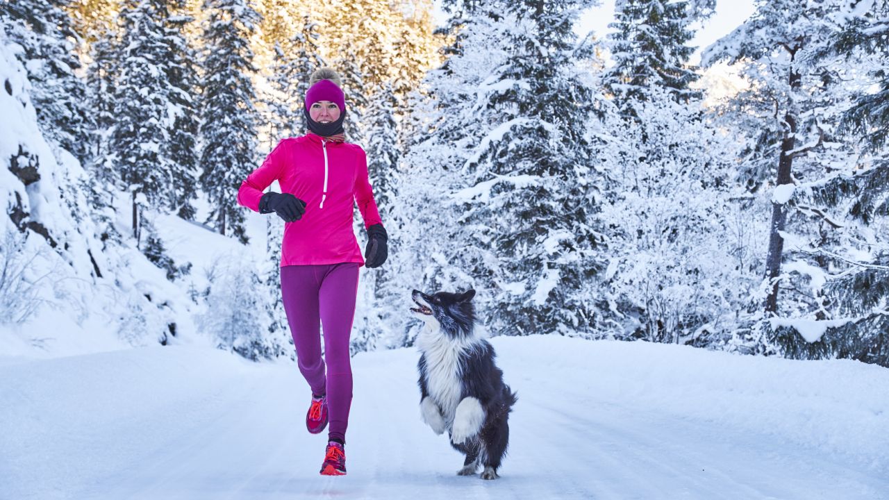 Nő fut kutyával a havas erdőben