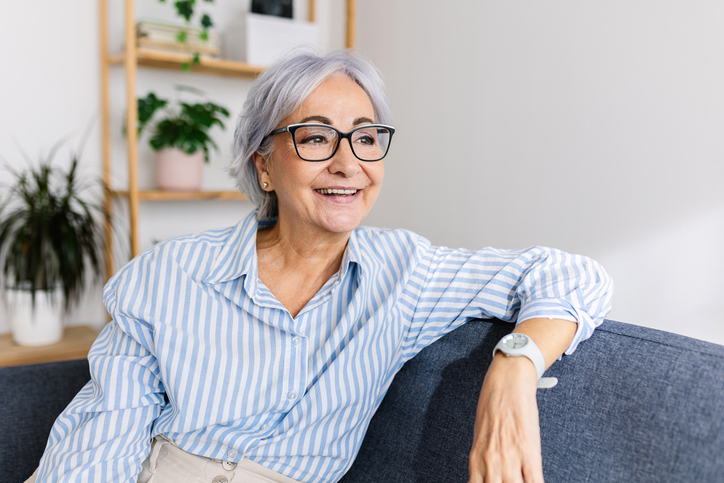 Mosolygó szemüveges hölgy ül a kanapén