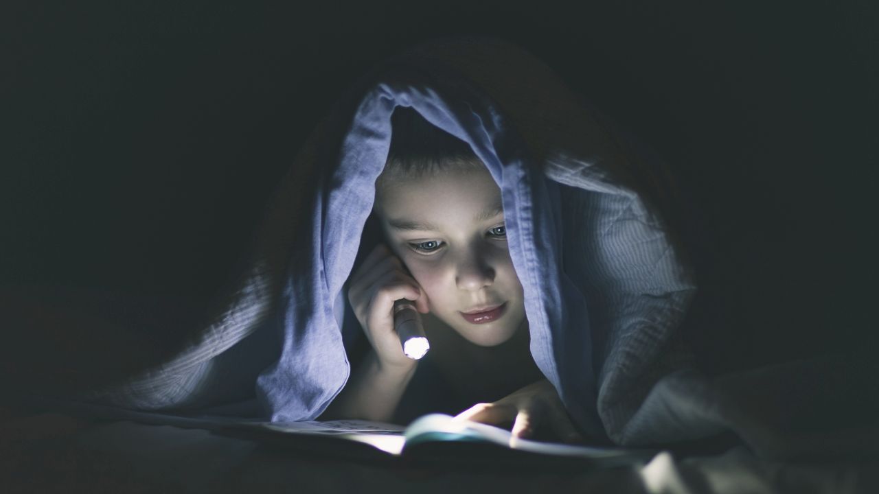 Kisfiú olvas a paplan alatt zseblámpával