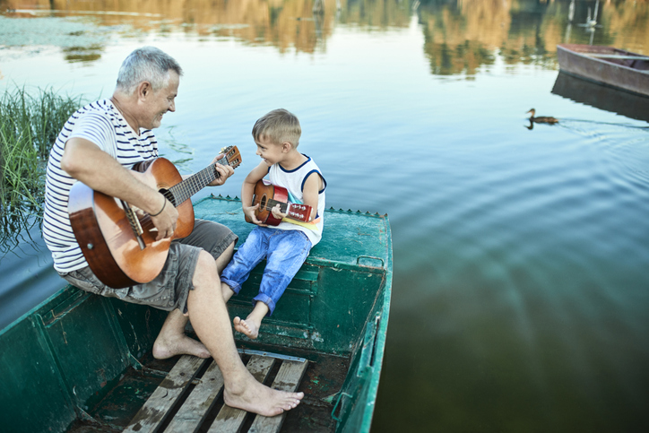 Nagypapa tanítja gitározni az unokát a stégen